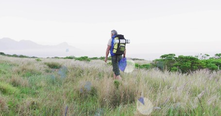 Walking mature adult hiker crossing golden grass field, with backpack, sleeping pad and boots