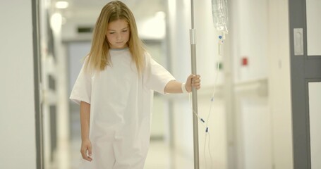 Walking gowned child holding IV pole through hospital hallway with corridor doors and wristband
