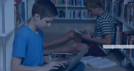 Typing student in blue t-shirt using laptop in library aisle, with books and tablet, copy space © vectorfusionart