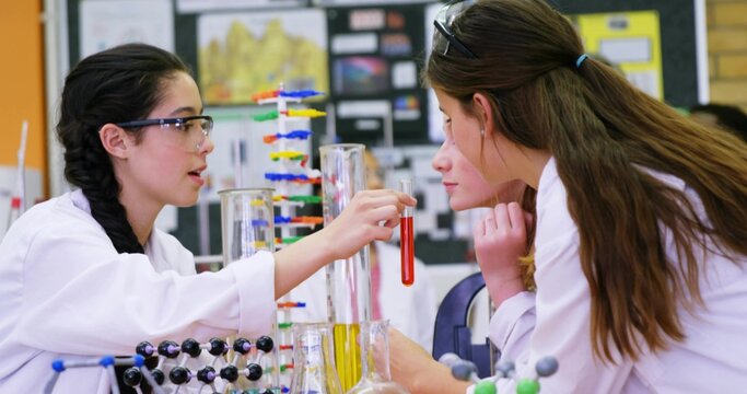 pupil in lab coat and goggles holding test-tube explaining in lab with molecular models, copy space