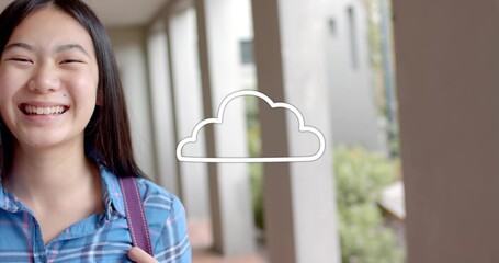 Smiling schoolgirl wearing blue shirt with backpack strap in campus walkway, cloud icon, copy space