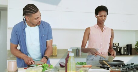 Slicing vegetables while stirring food couple in modern kitchen, with cutting board and frying pan