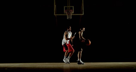 Dribbling basketball player facing defender on dimly lit hardwood court with hoop, wearing jerseys © vectorfusionart