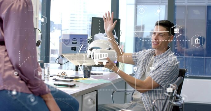 Man in striped shirt presenting VR headset to woman leaning on office desk, with monitors laptop