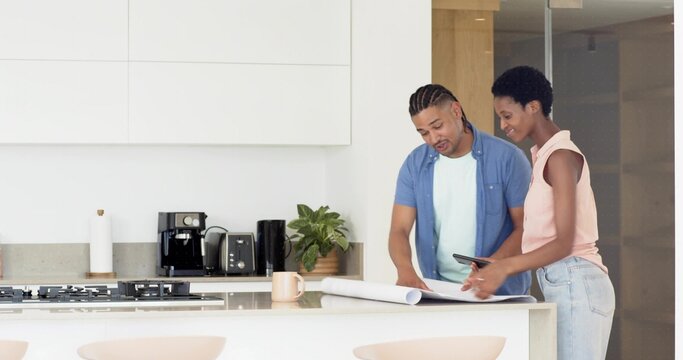 Reviewing homeowners planning renovation in modern kitchen, with blueprints and tablet
