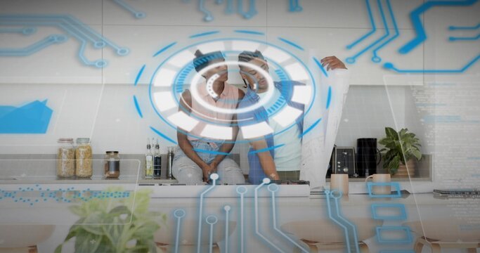 Gesturing couple wearing VR headsets using holographic interface in home kitchen, with blueprints