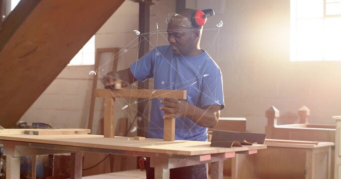 Mature woodworker wearing ear protection handling small wooden frame at workshop bench, with clamps