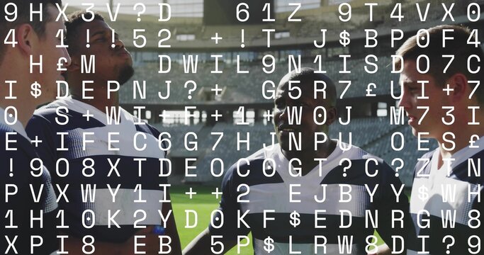 Huddling rugby players wearing striped jerseys discussing plan on grass pitch, with stadium beams