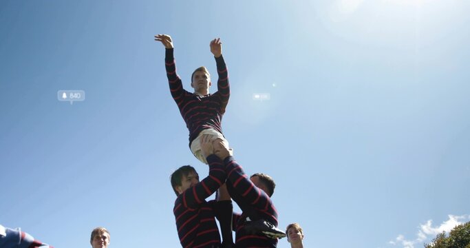 Lifting rugby teammate during lineout wearing striped jerseys, beige shorts on grass under blue sky