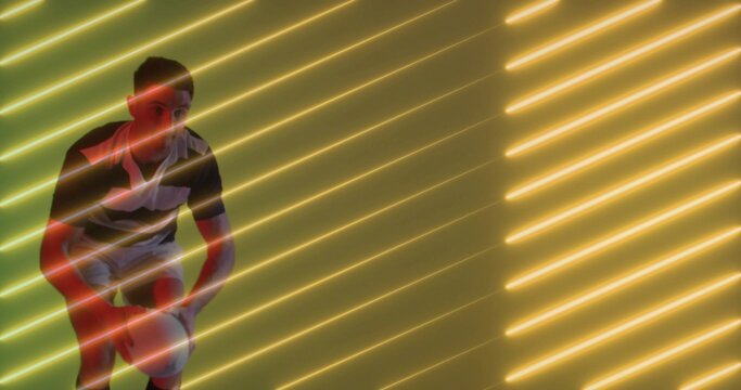 Male athlete in sportswear holding basketball in studio, with diagonal neon light tubes, copy space