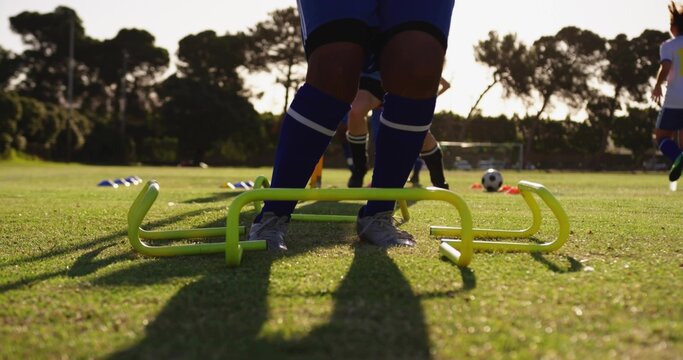 Soccer player feet stepping over neon agility hurdles in practice field, with cones and soccer ball - Powered by Adobe