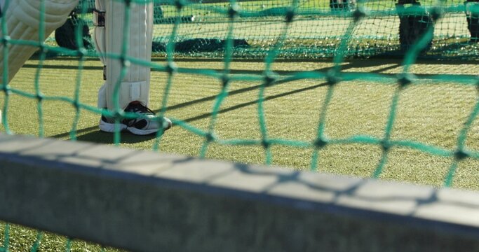 Cricket batter legs standing in net cage on turf, with leg pads, shoes, green net frame