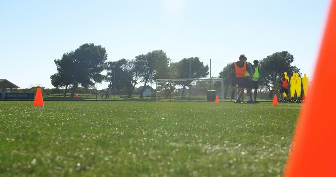 Practicing men wearing orange and neon bibs on soccer field, cones, mannequins, copy space - Powered by Adobe