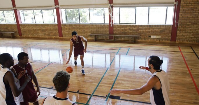 Dribbling adult male in maroon uniform moving across school gym court, holding orange basketball