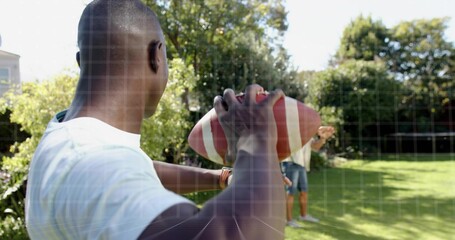 Holding man wearing white tee and denim shorts preparing to throw in backyard, with football, watch