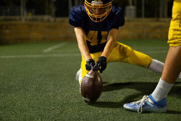American football player holding ball on field at night