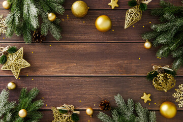 Golden baubles, pine branches and stars arranged on wooden surface with empty center. Festive Christmas background for seasonal greeting, invitation or design.