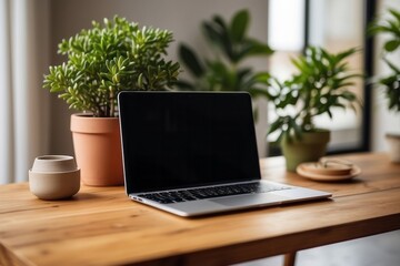 Fototapeta premium Wooden table with laptop blank white screen, complemented by a vibrant potted plant