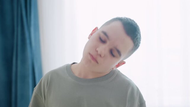 Close up of boy tilting head backward while performing neck stretch during flexibility training in softly lit home environment, intent posture shows effort and balance