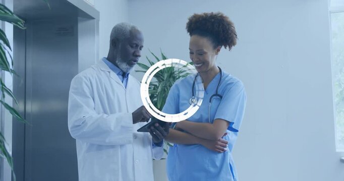 Doctor swiping records on tablet in hospital hall, loading icon showing, nurse pointing for review