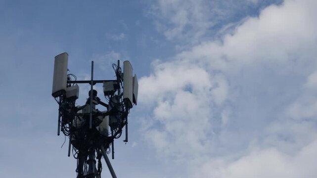Cellular telecommunications tower with antennas and equipment against blue sky with white clouds and power lines