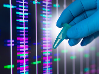 Gloved hand holding DNA sample with genomics analysis on screen