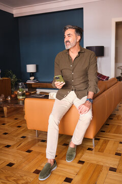 Man sitting on sofa holding phone and smiling in modern living room