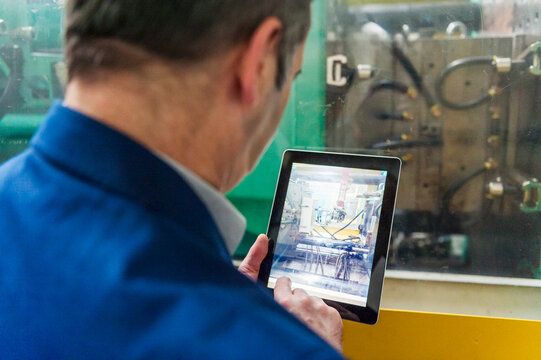 Employee monitoring plastic production machinery with tablet in factory