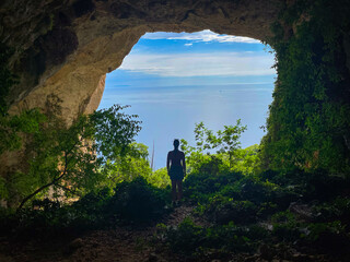 SILHOUETTE: Young female hiker explores a large coastal cave on Hvar island with a scenic view of blue Adriatic Sea. Freedom, discovery and the joy of exploring natural beauties of sunny Dalmatia.