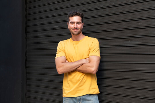 Smiling young man standing with arms crossed near shutter