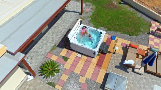 Aerial view around a mom and kids relaxing in a jacuzzi hot tub, sunny summer day