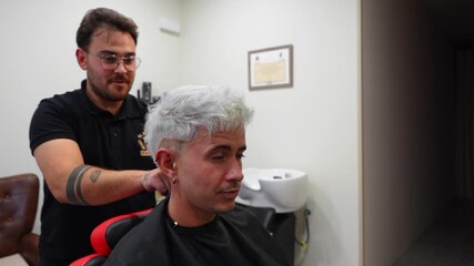 Hairdresser touches bleached hair while customer admires final result in the barbershop