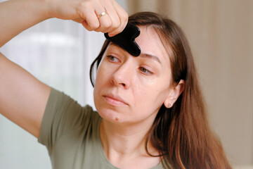 40s woman takes care of her face skin in the morning. She doing massage treatment for tensions with Gua Sha tool. Self facial care. Wellness, beauty and skincare routine. Healthcare projects