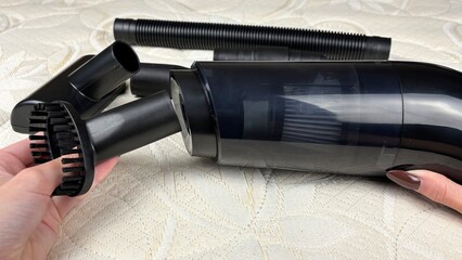 Woman's hand attaching a nozzle to a portable cordless vacuum cleaner against a white mattress....