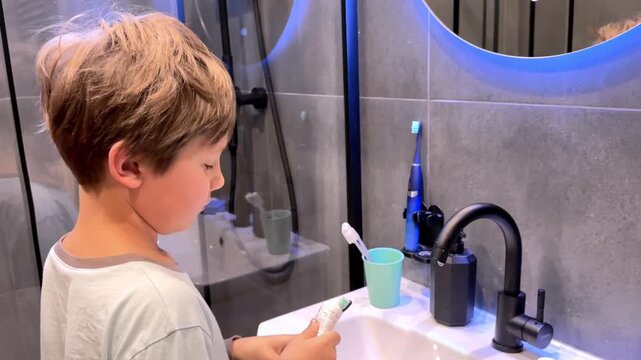 8-year-old boy in a modern bathroom squeezing toothpaste on toothbrush