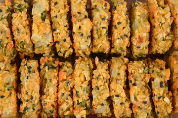 A close-up horizontal shot captures two neat stacks of baked, golden-brown vegan soy patties, revealing their chunky texture and black seeds