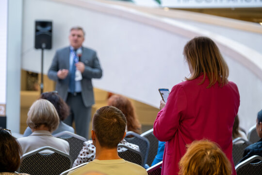 Audience gathers for presentation as speaker shares insights while woman in red records presentation on phone