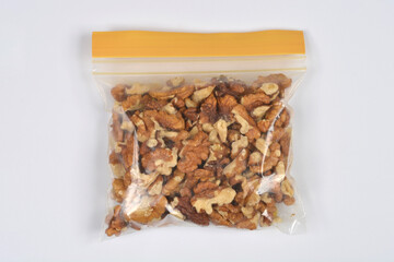 An overhead shot of a clear plastic zipper storage bag filled with shelled walnut pieces and halves, placed on a plain white studio background