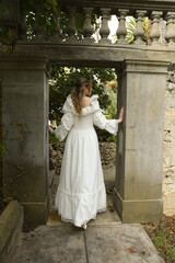 Fototapeta premium Full length female figure of beautiful blonde model wearing white fantasy wedding gown. walking through doorway of historical fairytale castle location 