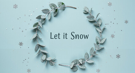 Circular eucalyptus wreath with text "Let it Snow" on blue background  