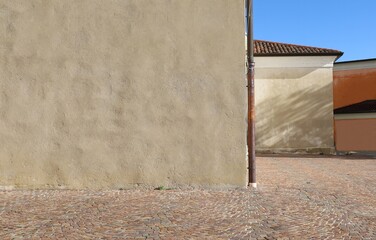 Rusty gutter at the corner of a cream colored plaster old wall. A orange wall, roof and sky on background. Porphyry pavement in front Background for copy space.