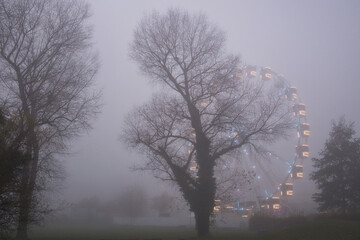 Beleuchtetes Riesenrad hinter B&auml;umen bei Nebel