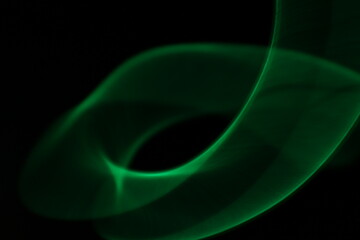 Abstract green light trails on dark background, long-exposure swirling motion lines for technology and energy background. Abstract green smoke or green fire on dark background. Green gas fire abstract