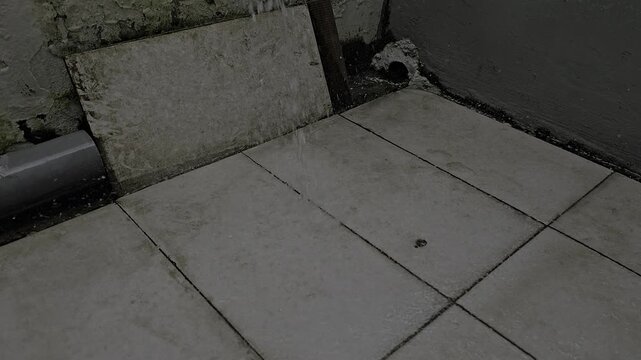 Water streams onto aged tile floor in a dimly lit corner, creating a sense of neglect and decay with its worn texture and dark ambiance