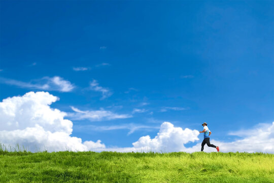 Running into Clarity: A solitary figure, a runner, strides purposefully across a vibrant, green landscape beneath a breathtaking, blue sky dotted with puffy, white clouds, embodying freedom.