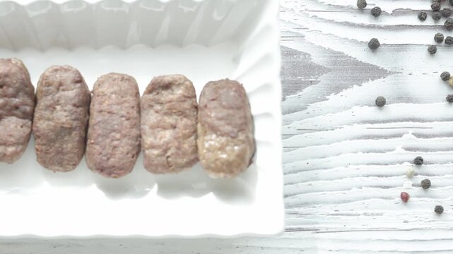 Close-Up of Romanian Mici Sausages Served with Flatbread and Tomatoes on a White Plate	