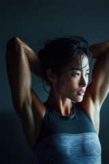 Candid shot of asian woman rotating shoulders before workout indoors, dim gym lighting with soft side glow from window, athletic warm-up routine captured naturally, fitness lifestyle concept