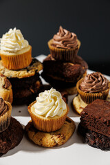 Chocolate and vanilla frosted cupcakes rest atop stacked cookies in a creative dessert arrangement on a white surface, with a blurred gray background and copy space