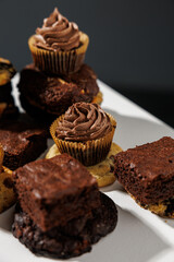 Chocolate and vanilla frosted cupcakes rest atop stacked cookies in a creative dessert arrangement on a white surface, with a blurred gray background and copy space