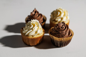Overhead view of four cupcakes—two chocolate, two vanilla—casting long shadows on a white surface under bright natural light, with copy space